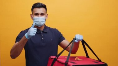 Yüz maskeli ve eldivenli Hintli bir adam yemek poşetini kaldırıyor ve başparmağını kaldırıyor.