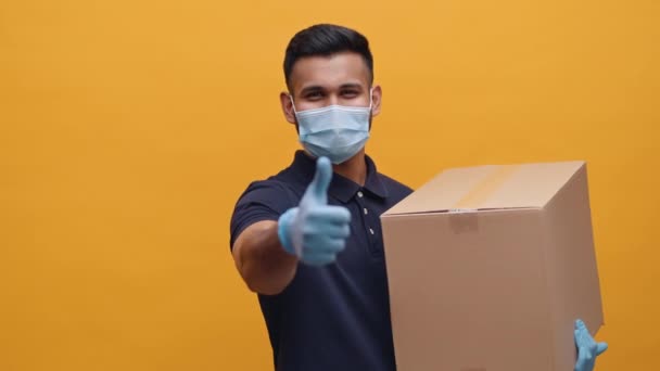 Ung man med ansiktsmask och handskar som håller i förpackningen och visar tummen upp — Stockvideo