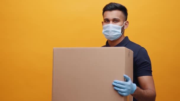 Young indian man holding big cardboard box and nodding his head. wearing face mask and gloves — Stock Video