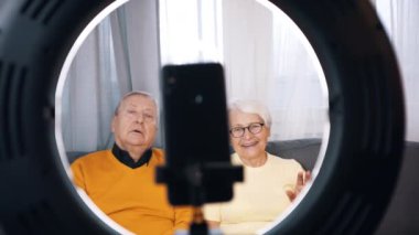 Yaşlı bir çift aile için röportaj yapıyor ya da video mesajı kaydediyor. Akıllı telefon kamerasına el sallayan kadın