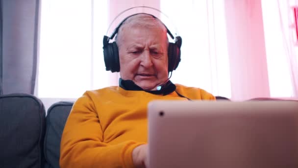 Retrato de anciano con auriculares jugando juegos en el portátil — Vídeos de Stock