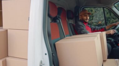 Paketlerle dolu minibüste otururken teslimatçı tabletin sipariş listesini kontrol ediyor.