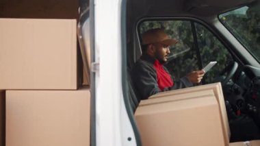 Paketlerle dolu minibüste otururken tablette Hint kuryesi sipariş listesini kontrol ediyor.