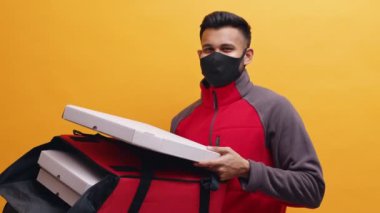 Yüzü maskeli genç teslimatçı müşteriye pizza getiriyor.