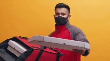Coronavirüs salgını sırasında pizza teslimatı. Yüzü maskeli adam müşteriye pizza kutusu veriyor.