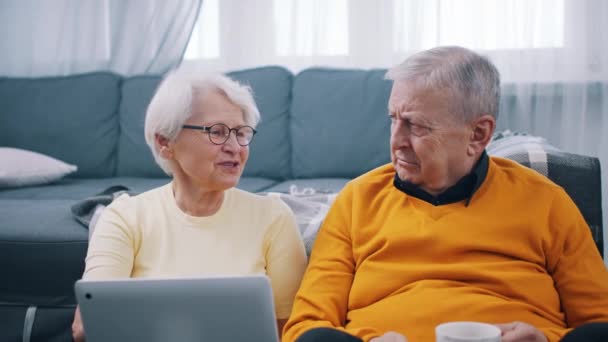 Літня пара на пенсії використовує ноутбук у приміщенні та розслабляється на підлозі — стокове відео