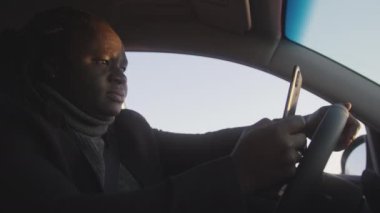 Genç Afrikalı Amerikalı siyah adam araba kullanırken akıllı telefon kullanıyor.
