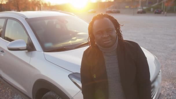 Ung afrikansk amerikansk mand nikker med hovedet foran sin nye bil på vejen ved solnedgang – Stock-video