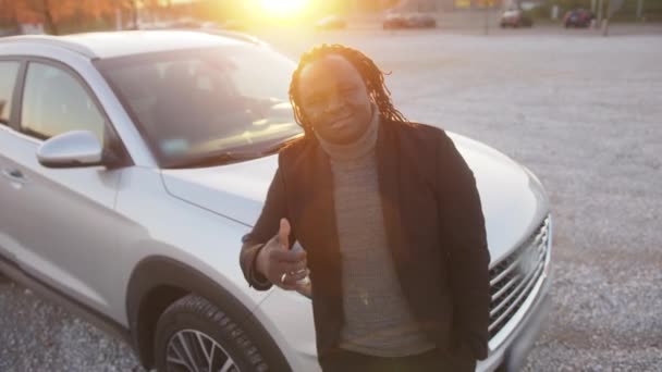 Молодий афроамериканець, який показує великий палець перед своєю новою машиною на заході сонця. — стокове відео