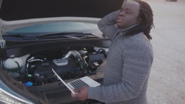 Jeune homme noir afro-américain bouleversé réparer la voiture tout en utilisant un ordinateur portable — Video