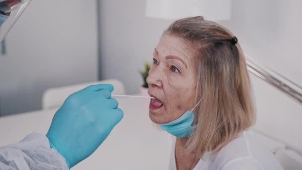 Doktor yaşlı kadından tükürük örneği alıyor. Covid-19 önlemi — Stok video