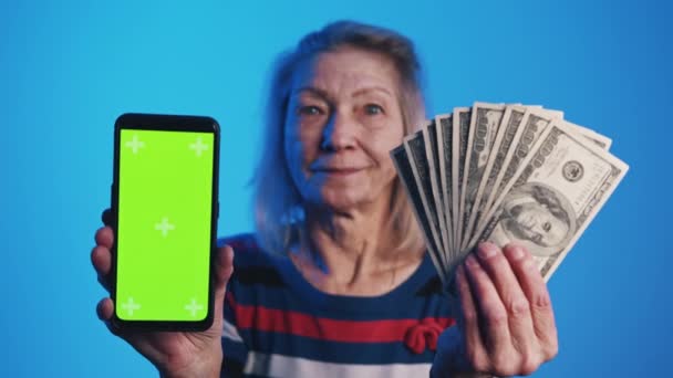 Ηλικιωμένη γυναίκα κρατώντας smartphone με πράσινη οθόνη και χρήματα. Επενδυτική εφαρμογή — Αρχείο Βίντεο
