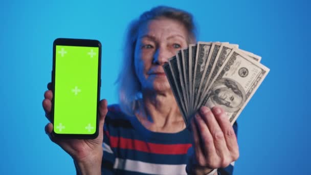 Mujer mayor sosteniendo smartphone con pantalla verde y dinero. Aplicación de inversión — Vídeos de Stock
