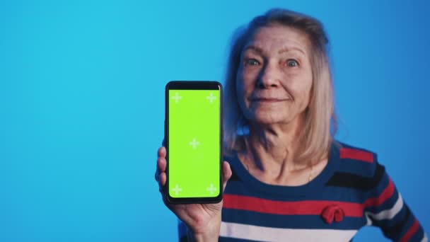 Gammal kvinna med vidöppna ögon håller smartphone med grön skärm — Stockvideo