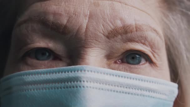Närbild på blå ögon gamla grå hår kvinna med ansiktsmask. Sårbar åldrad person och covid19 — Stockvideo