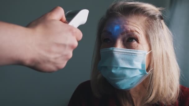 Digitales Thermometer zur Messung der Körpertemperatur einer älteren Frau mit medizinischer Maske — Stockvideo