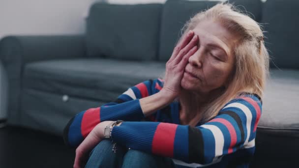 リビングルームの床に座って頭痛に苦しんでいる高齢者の女性 — ストック動画