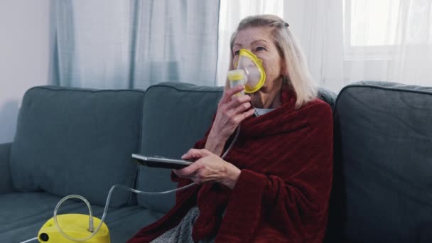 Mujer anciana vulnerable en cuarentena usando inhalador de oxígeno y cambiando los canales en la televisión — Vídeo de stock