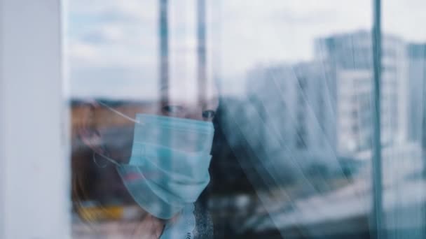 Portrait of lonely elderly woman in quarantine with face mask looking through the window — Stock Video