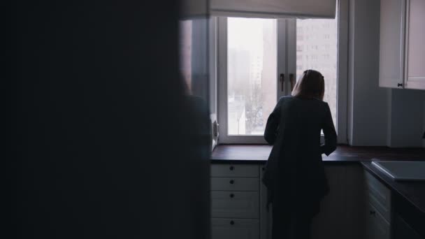 Seorang wanita tua yang kesepian bersandar di lemari dapur dan melihat melalui jendela — Stok Video