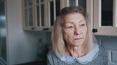 Üzgün, yaşlı, gri saçlı kadın pencereden bakıyor. Karantinada savunmasız kişi