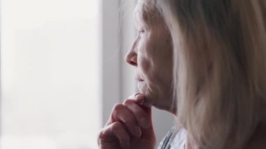 Üzgün, yalnız 70 yaşında, pencereden bakan yaşlı bir kadın.