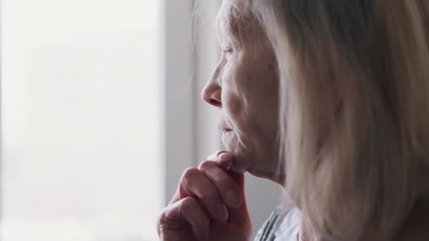 Trieste eenzame 70-jarige senior vrouw die door het raam kijkt — Stockvideo