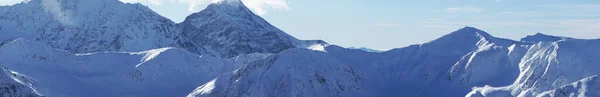 Panoramatický záběr na vrchol hory přikrytý sněhem s modrou oblohou v pozadí — Stock fotografie