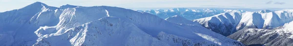 Πανοραμική βολή του βουνού κορυφής που καλύπτεται στο χιόνι με μπλε ουρανό στο παρασκήνιο — Φωτογραφία Αρχείου