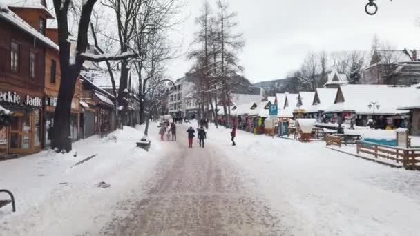 Sněhem pokrytá ulice s chodícími lidmi. Kavárny na jedné straně se zasněženými lavicemi — Stock video