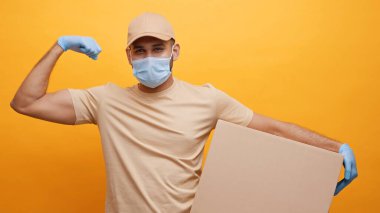 Yüzü maskeli güçlü genç kurye. Karton kutuyu bükerken kaslarını kasıyor.