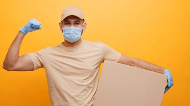 Yüzü maskeli güçlü genç kurye. Karton kutuyu bükerken kaslarını kasıyor.