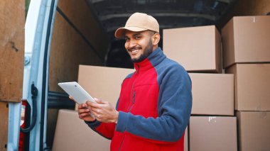 Siparişlerin önizlemesi için tablet kullanan teslimatçı. Paketlerle minibüsün önünde dikiliyorum.