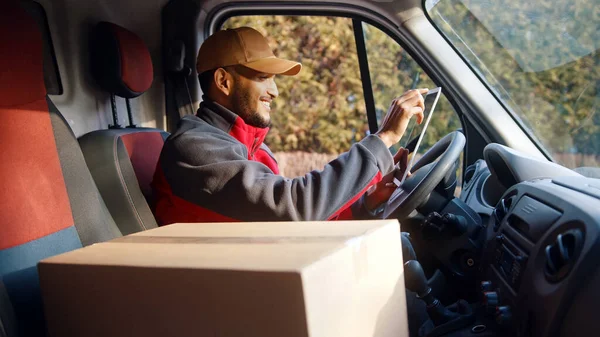 Delivery driver looking at tablet and then outside to confirm delivery address