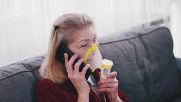 Femme âgée utilisant un inhalateur d'oxygène tout en parlant au téléphone. Éclosion de coronavirus et groupe vulnérable de personnes — Video