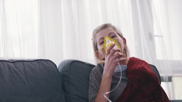 En äldre kvinna som använder syrgasmask hemma. Behandling av allergi eller lungsjukdom. — Stockvideo