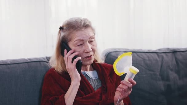 Eenzame oudere vrouw met zuurstof inhalator en telefoon conversie. Covid19 pandemie — Stockvideo