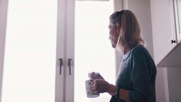 Depressieve en eenzame oude vrouw mengen suiker in haar koffie, terwijl het kijken door het raam — Stockvideo