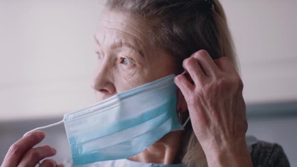 Portret van een oude vrouw die binnen een gezichtsmasker opzet — Stockvideo