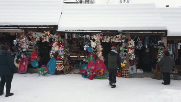 Snow-covered small shops with people wearing winter clothes and busy shopping. — стоковое видео