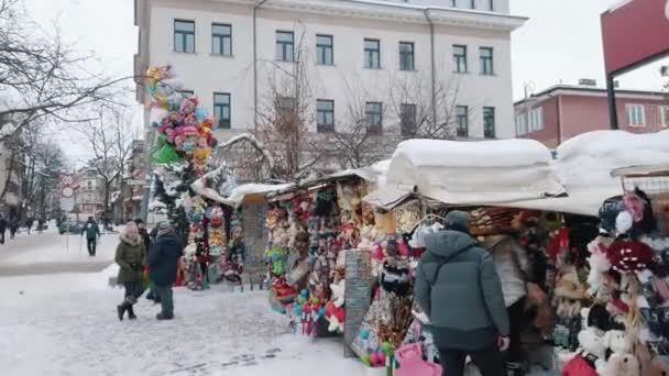 Туристы возле торговцев продают игрушки - Заснеженная улица с деревьями и домами — стоковое видео
