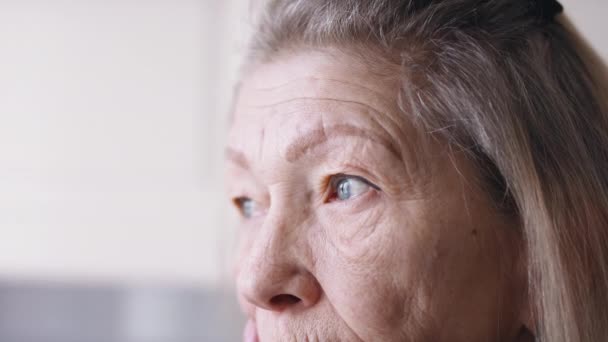 閉じるアップ上の青い悲しい目の孤独な高齢者の女性を通して窓を見て — ストック動画