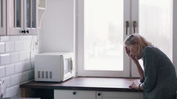 Débil anciana solitaria apoyada en el mostrador de la cocina y mirando por la ventana — Vídeo de stock