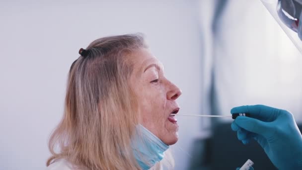 Nero medico in uniforme completa esecuzione tampone nasale covid tes su una donna anziana — Video Stock