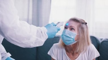 Vücut ısısı ölçümü. Lazer temassız termometre. Coronavirus sırasındaki yaşlı bir kadının vücut ısısını ölçen doktor.