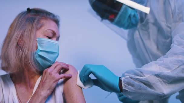 Dokter geeft Covid vaccin aan oudere vrouw met gezichtsmasker. Vaccinatie en immunisatie tijdens het coronavirus — Stockvideo