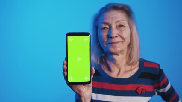 Oude vrouw met smartphone met groen scherm en knikkende kop — Stockvideo