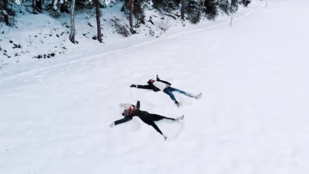 Jeune couple romantique en voyage de vacances d'hiver. Faire des anges de la neige sur grand champ. — Video