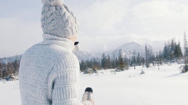 Genç bayan kış tatilinde dağda. Termal şişeden sıcak içecek içmek ve kar yağışının tadını çıkarmak.