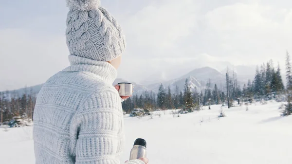 Młoda kobieta na zimowych wakacjach w górach. Picie gorącego napoju z butelki termalnej i cieszenie się opadami śniegu — Zdjęcie stockowe